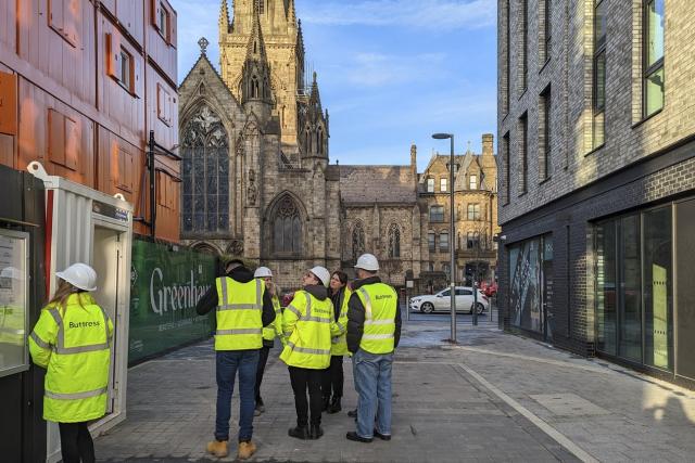 a groups of architects in hi vis jackets visit site. there is a view of salford cathedral down the side of the project.