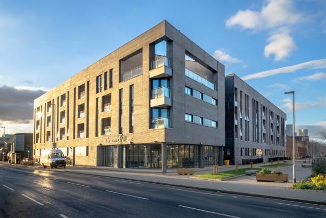 a view of a 4 storey building of grey brick, the afternoon light catches one face making it glow golden