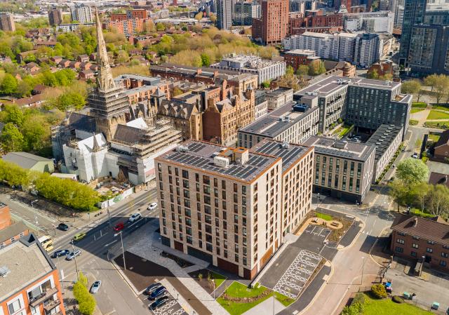 an aerial view of apartments made from buff brick salford cathedral is in the background