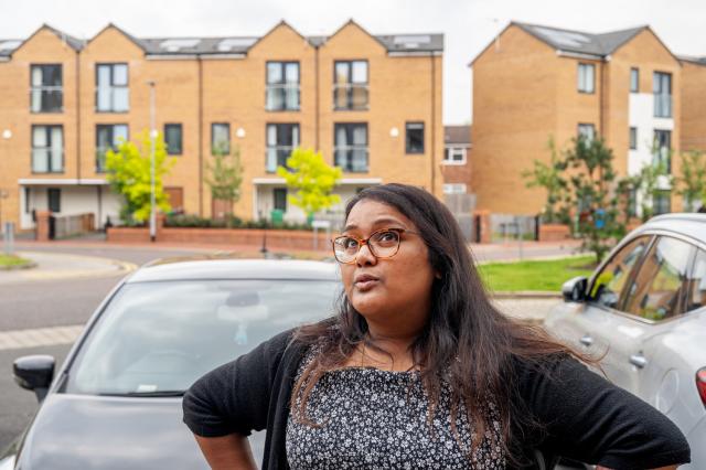 A lady stands with her hands on her hips with new brick houses in the background.