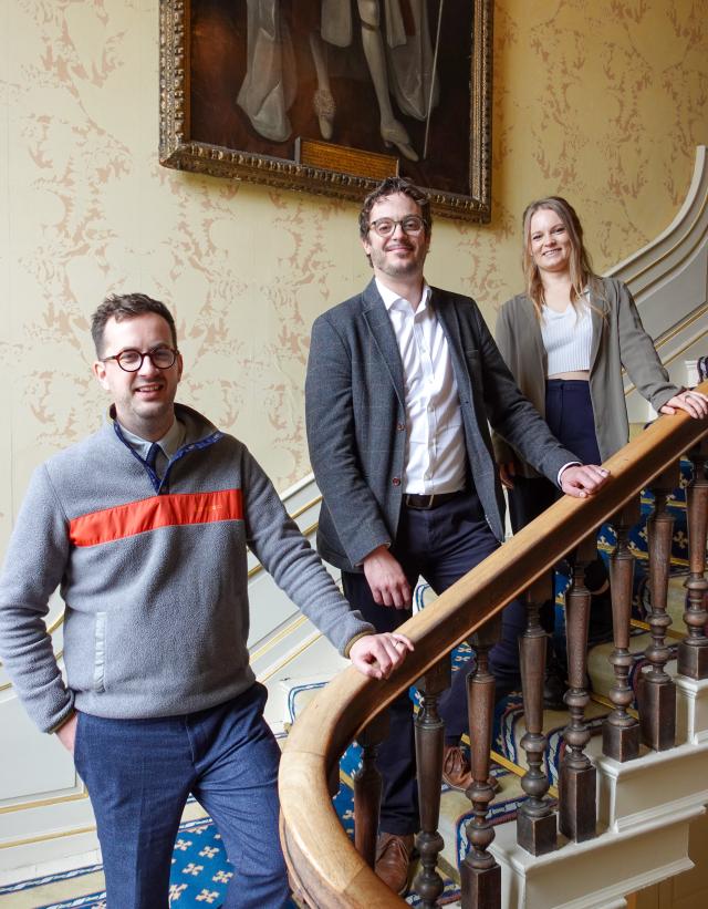 Three people standing on stairs, holding onto a wooden banister