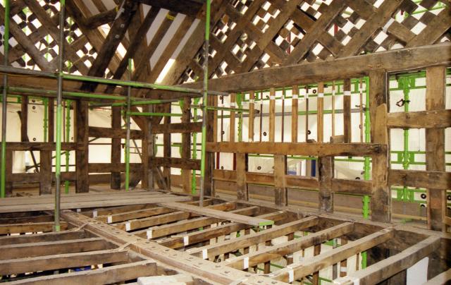 An interior image of timber frame supported by green scaffolding.