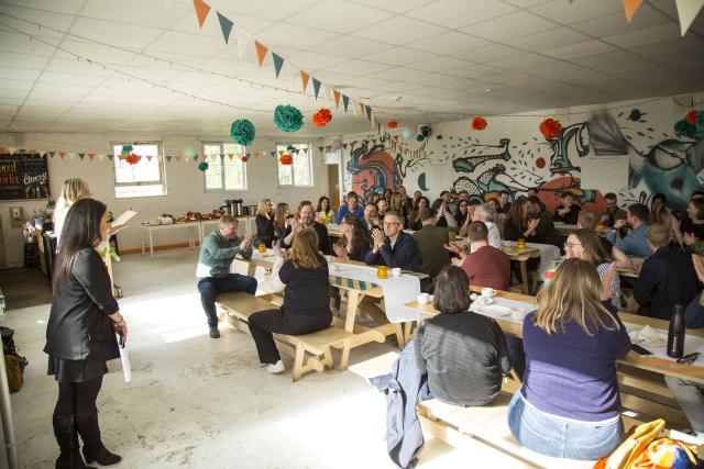 A group image of people sat on benches in a room.