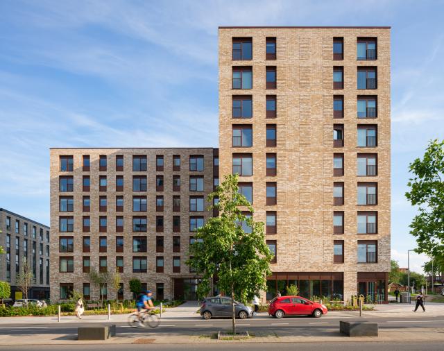 Greenhaus - a brick mid-rise building with a red car driving in front of it
