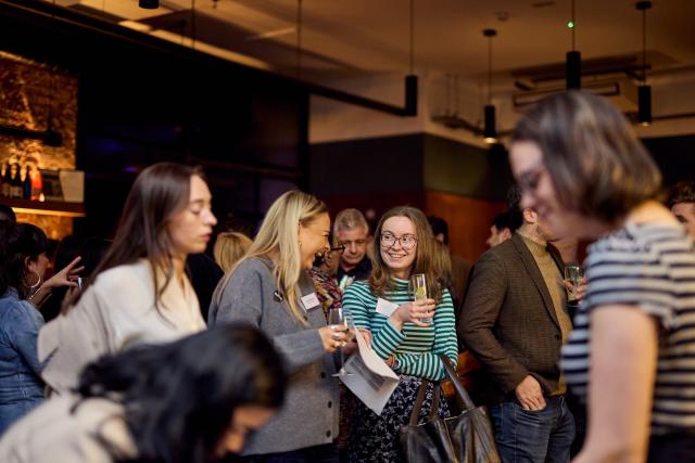 A group photo at an event in a bar. Two girls in the centre of the photo talking.