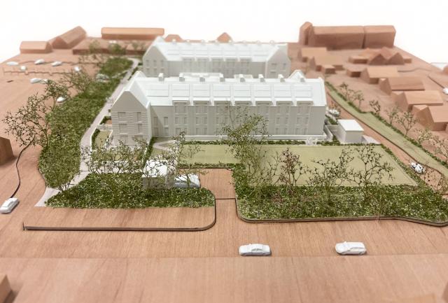 an architectural model from above. the landscape is timber with the buildings in white and landscape in green