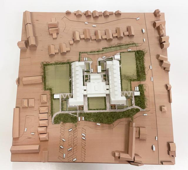 an architectural model from above. the landscape is timber with the buildings in white and landscape in greenn