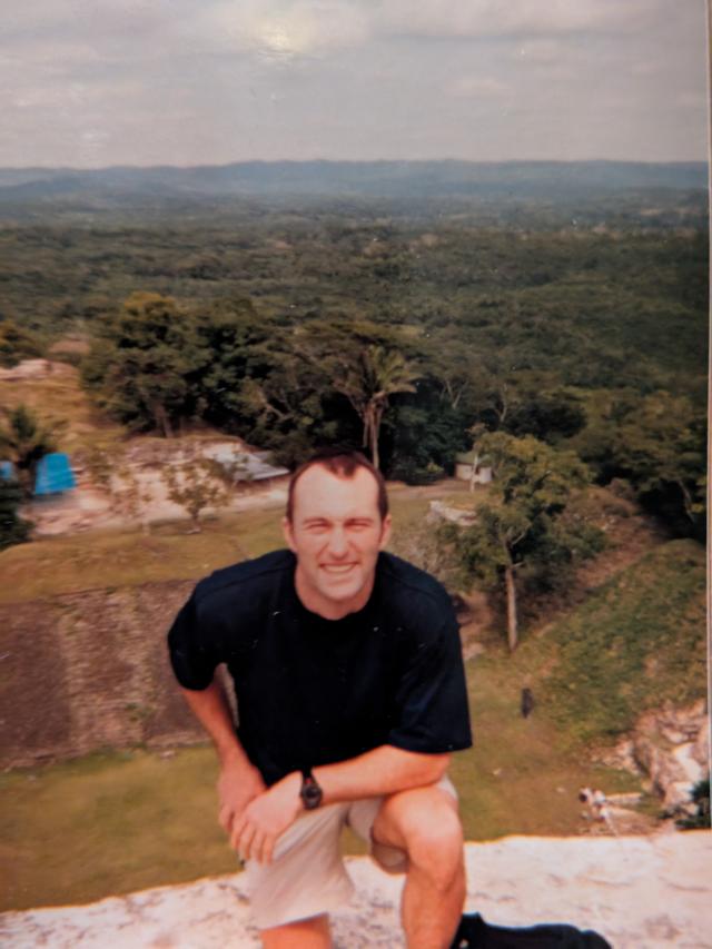 A man kneeling on a rock in front of the countryside.