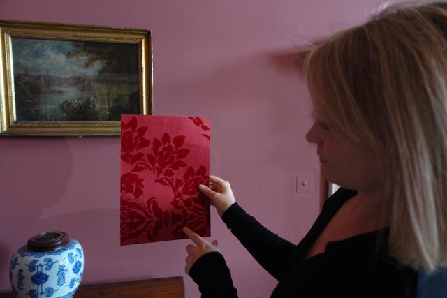 Hannah Bellerby, a woman with blonde hair, holding a piece of red wallpaper