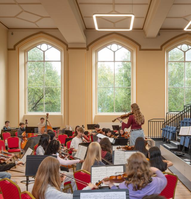 A group of students playing musical instruments in performance space/hall.