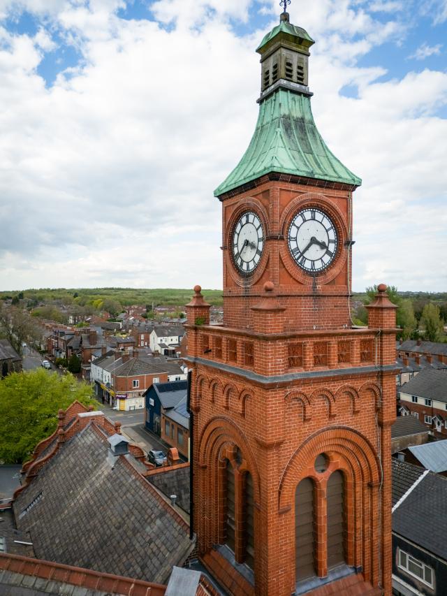 A red brick clock tower with green pitched roof.