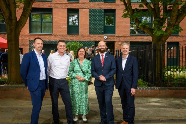 A group of four men and one woman outside an apartment block, with trees in the background.