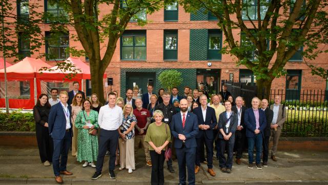 A large group of people stood outside an apartment block, with trees outside.